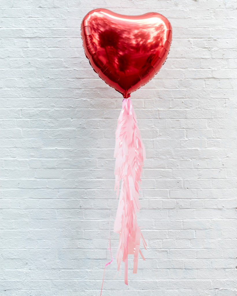 A red jumbo heart-shaped foil balloon with crepe streamer fringe tail