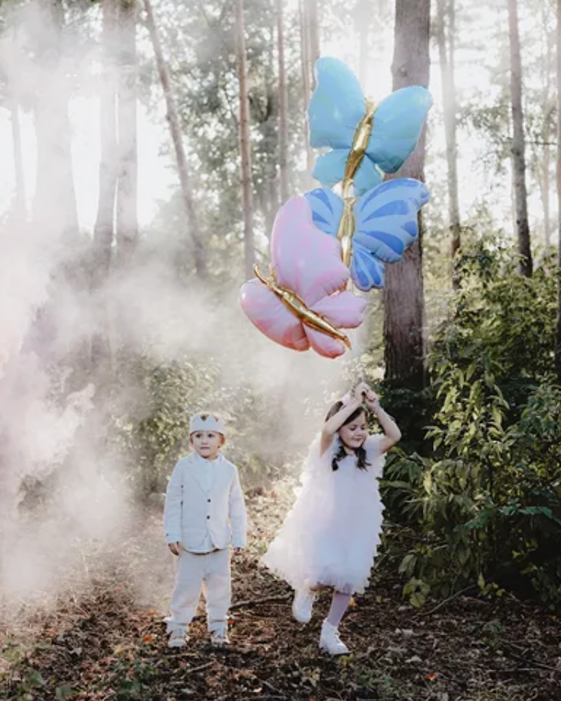 Two children in a forest with butterfly-shaped balloons.