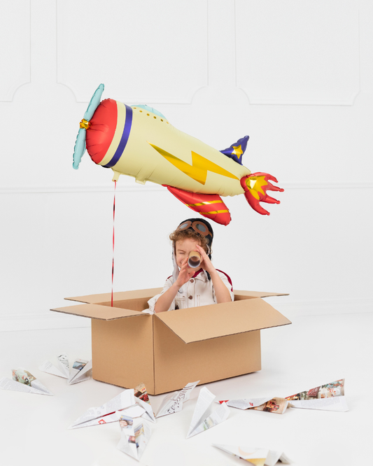 Child playing with a cardboard box and airplane balloon on a white background