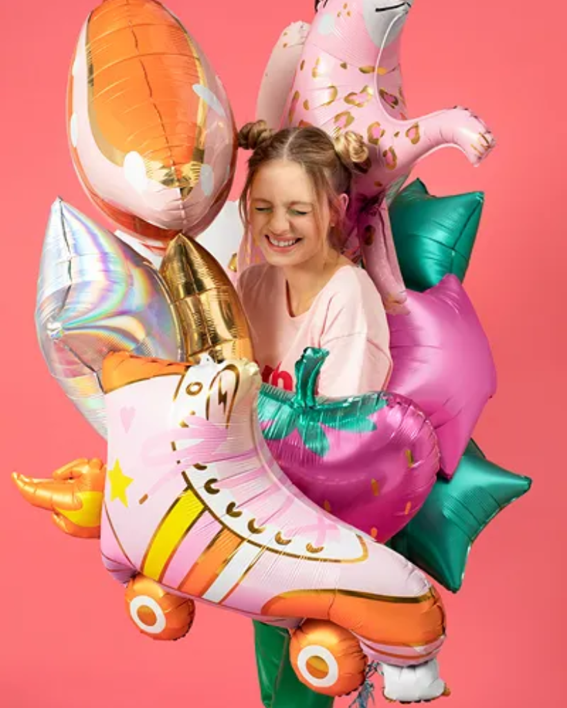 Person holding colourful inflatable balloons against a pink background