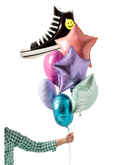 Colorful balloons including a black shoe with a smiley face, held by a person wearing a checkered shirt.
