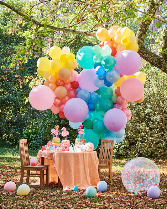 pastel rainbow party decorations and balloon garlands in a park setting