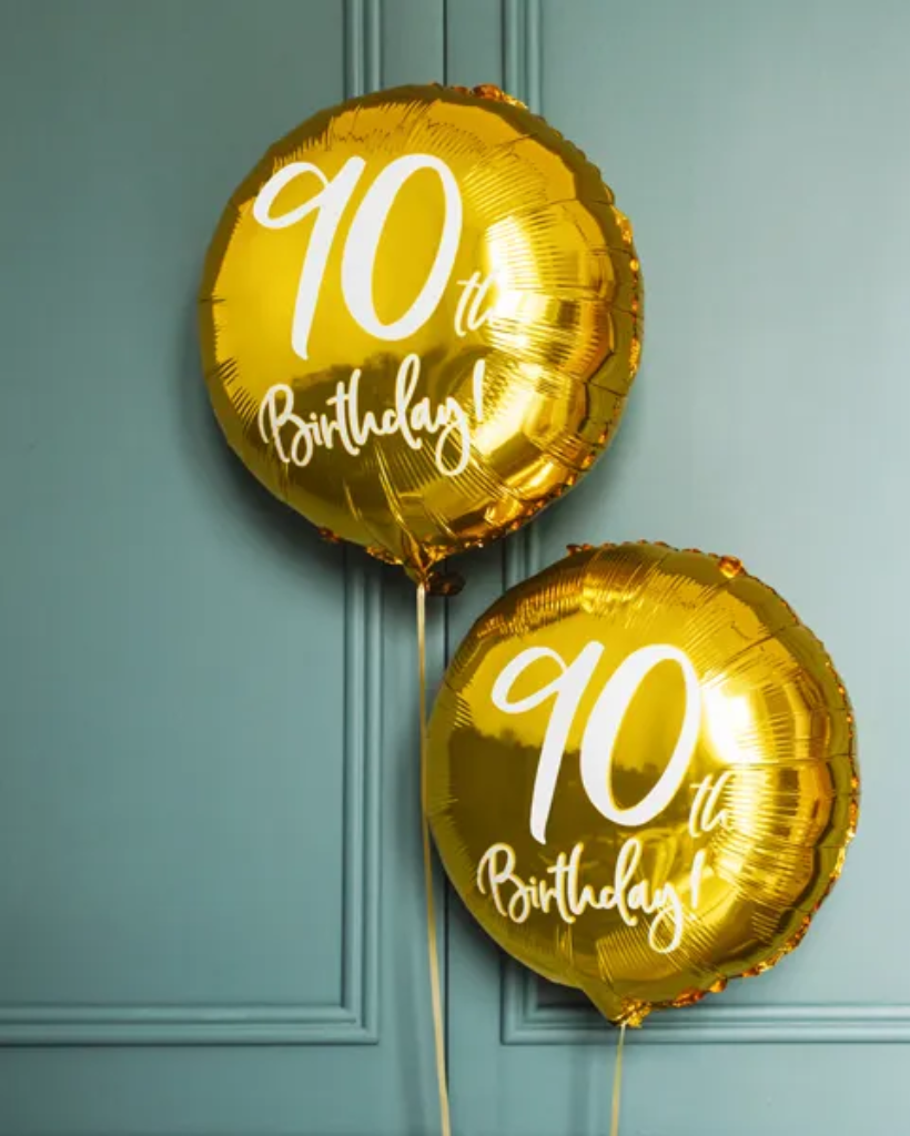 Two gold '90th Birthday' balloons against a teal background