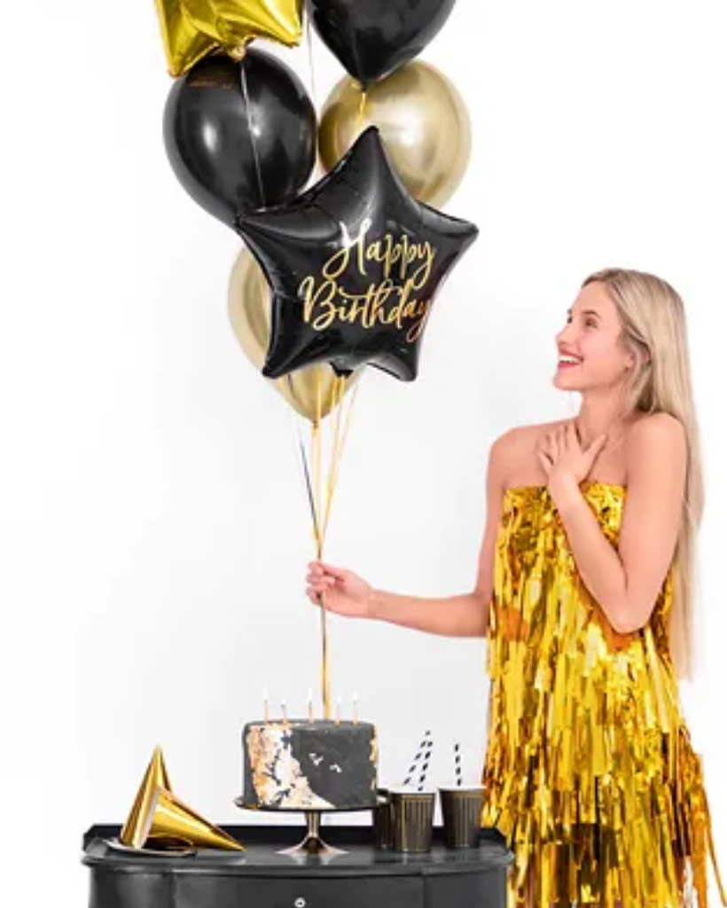 Woman in a gold dress holding birthday balloons with a cake on a white background
