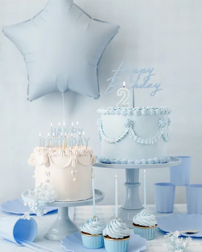 Two birthday cakes with candles and a star-shaped balloon against a light gray background.