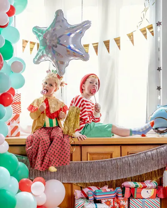 Two children in clown costumes sitting on a table with balloons and decorations.
