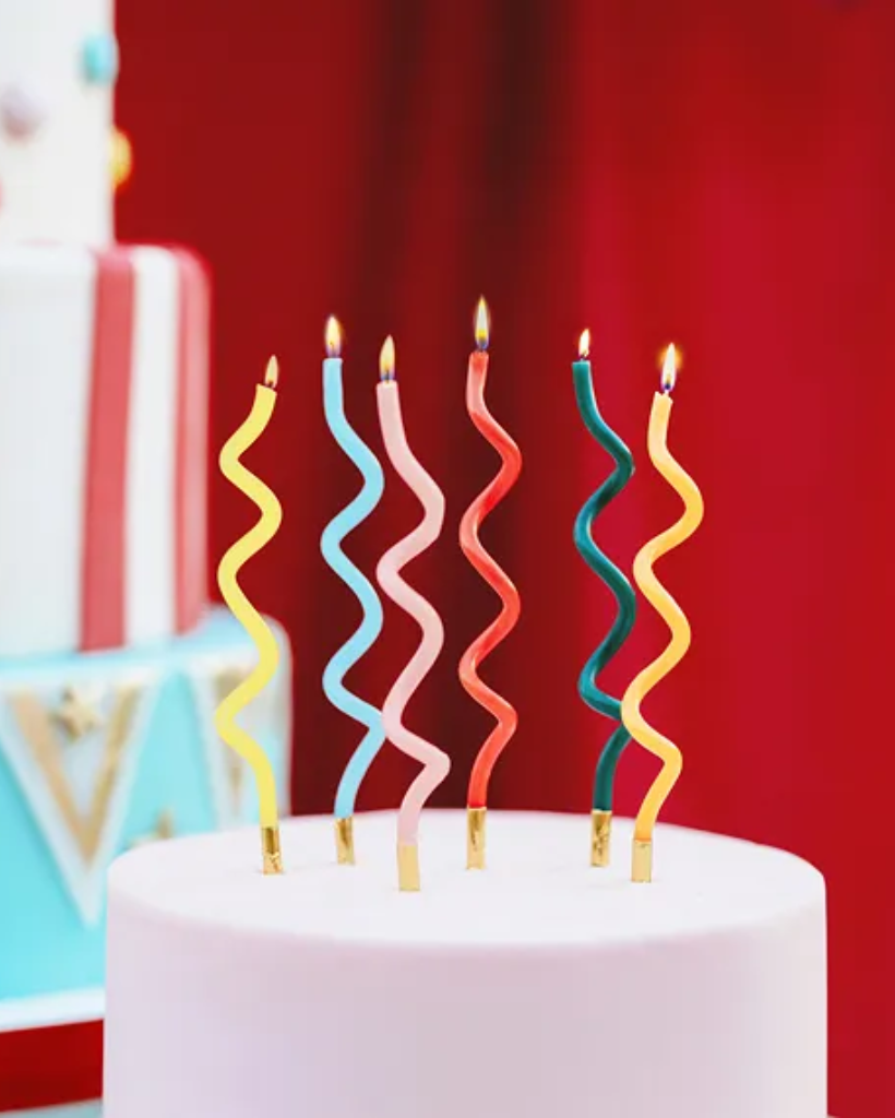 Colorful wavy birthday candles on a cake with a red curtain background