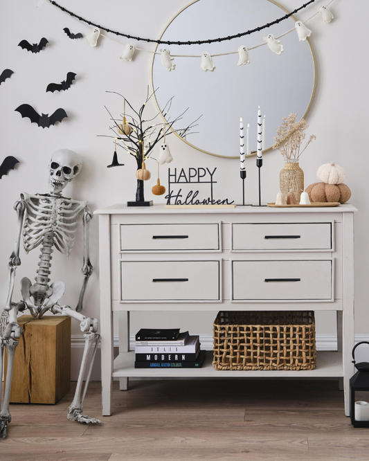 Halloween-themed room decor with skeleton, pumpkins, and decorations on a white dresser.