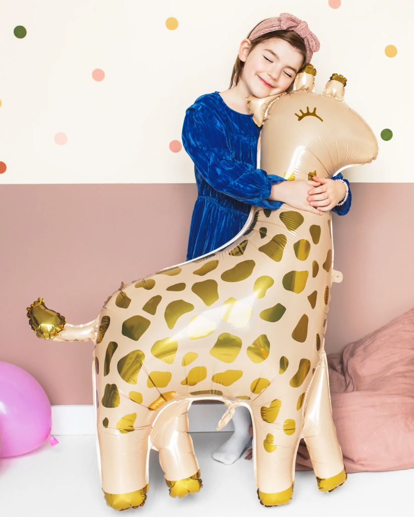 Child hugging a large inflated giraffe balloon with a polka dot background