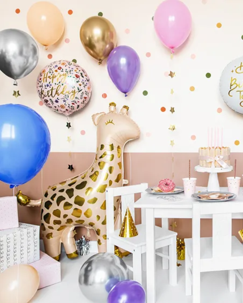 Children's birthday party setup with balloons, a giraffe foil, and a table with cake and plates.