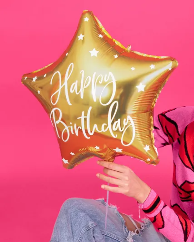 Gold star-shaped balloon with 'Happy Birthday' text held by a person against a pink background