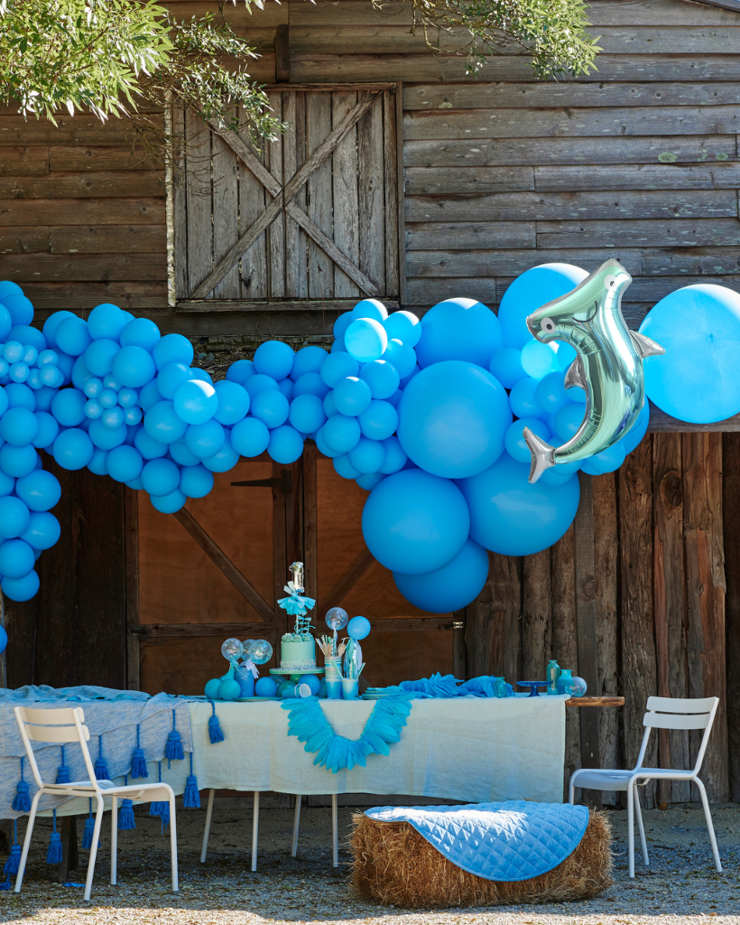 Decorative setup with blue balloons and a hammerhead shark balloon in front of a wooden building.