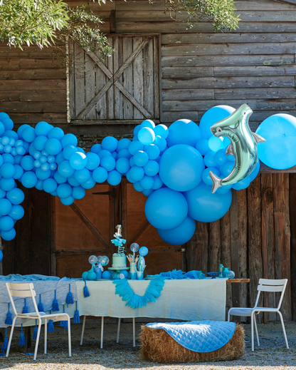 Decorative setup with blue balloons and a hammerhead shark balloon in front of a wooden building.