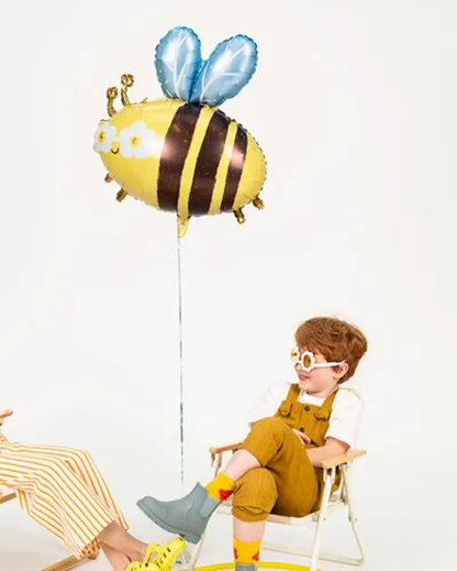 Child sitting on a chair with a bee-shaped balloon against a white background