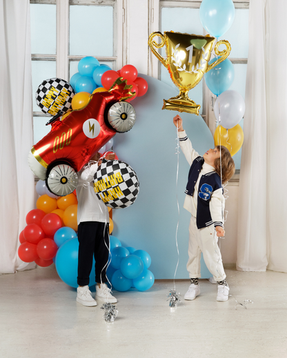 Two children playing with colorful balloons and a trophy in a room with large windows.