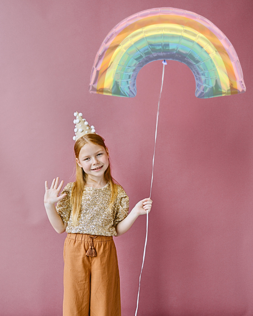 Child holding a rainbow-shaped balloon against a pink background