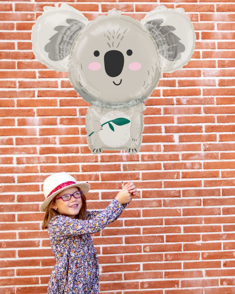 Child holding a large balloon shaped like a koala against a brick wall