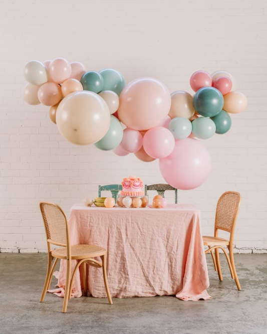 Decorative balloon arch over a table with a cake and chairs in a room.