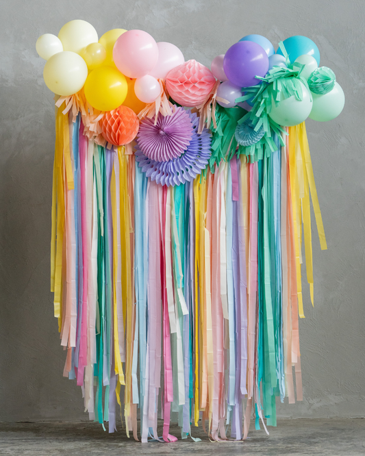 Colorful balloon and ribbon arch against a gray wall