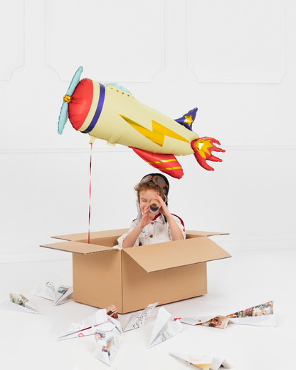 Child playing with a cardboard box and airplane balloon on a white background