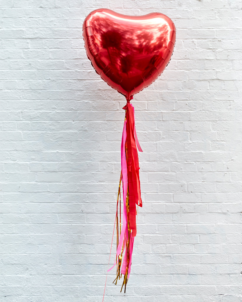 A shiny red jumbo heart-shaped foil balloon with streamer tails, inflated and displayed against a plain background.