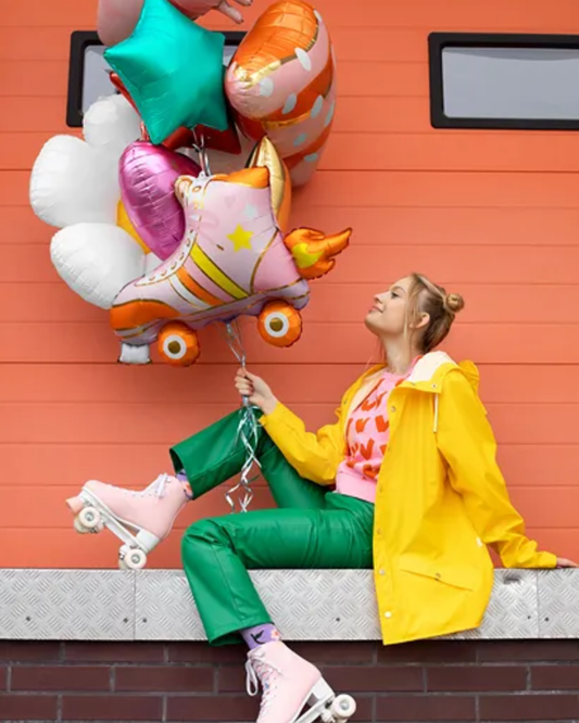 Person in a yellow raincoat holding colorful balloons against an orange wall.