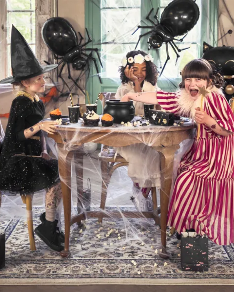 Children in Halloween costumes sitting around a table with decorative elements.