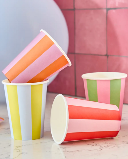 Colorful striped paper cups on a marble surface with a pink tiled wall background