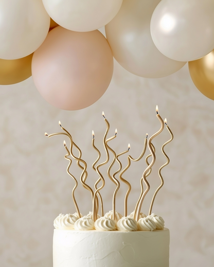 Decorative cake with wavy gold candles and balloons in the background