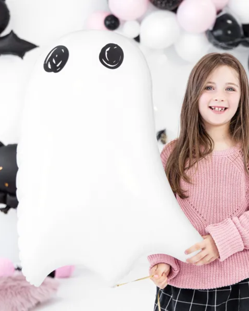 Young girl holding a large white ghost foil balloon with black accents against a balloon background