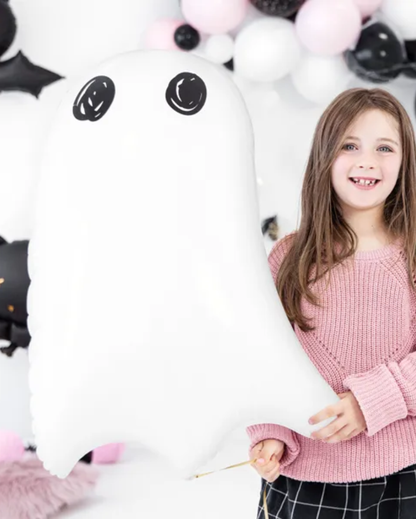 Young girl holding a large white ghost foil balloon with black accents against a balloon background
