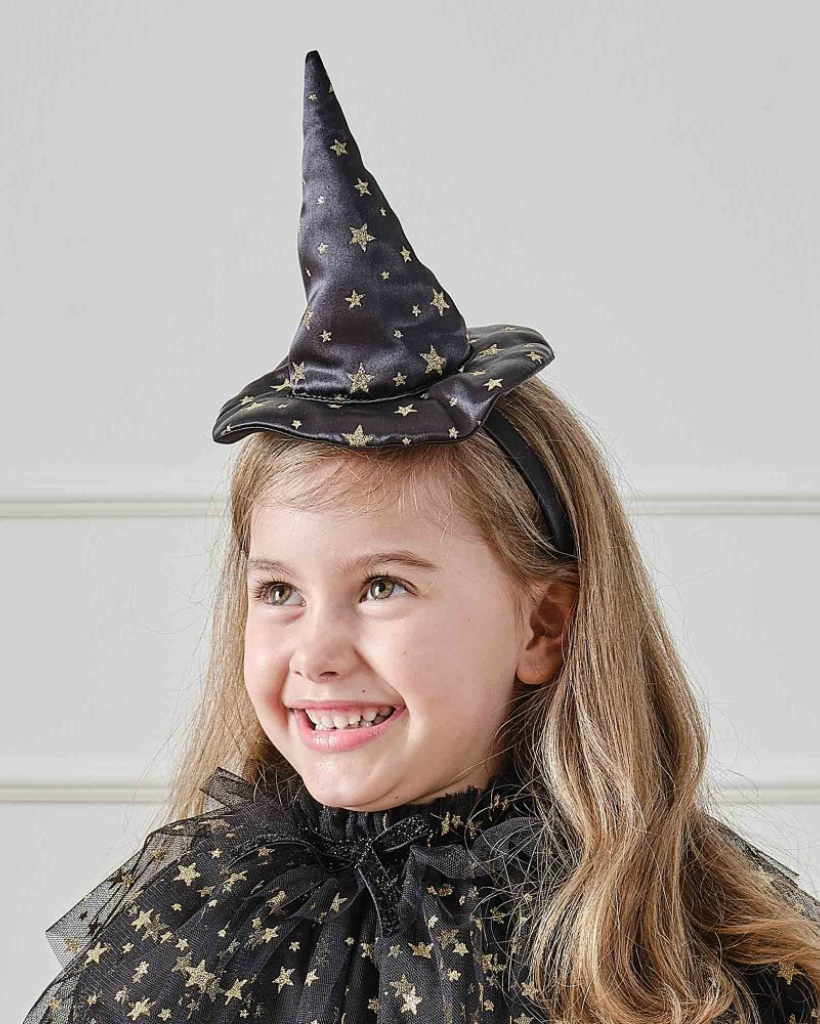 A child with long light brown hair wearing a black witch hat with gold stars and a matching black tulle cape with gold stars