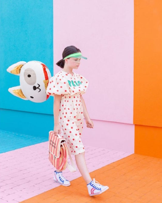 Person wearing a polka dot dress with a colourful geometric background holding a dog head balloon