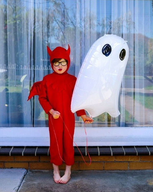 child in devil halloween costume holding a white ghost foil balloon