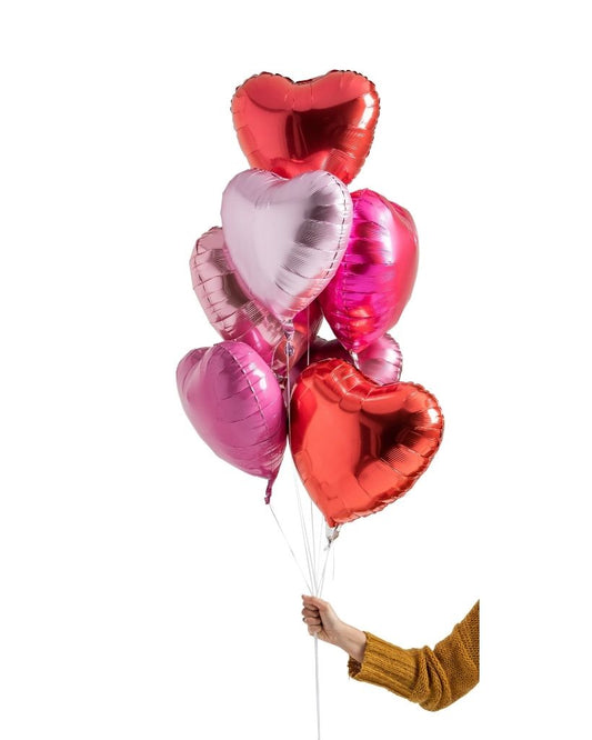 A set of heart-shaped foil balloons in shades of pink and red, held by a person against a white background.