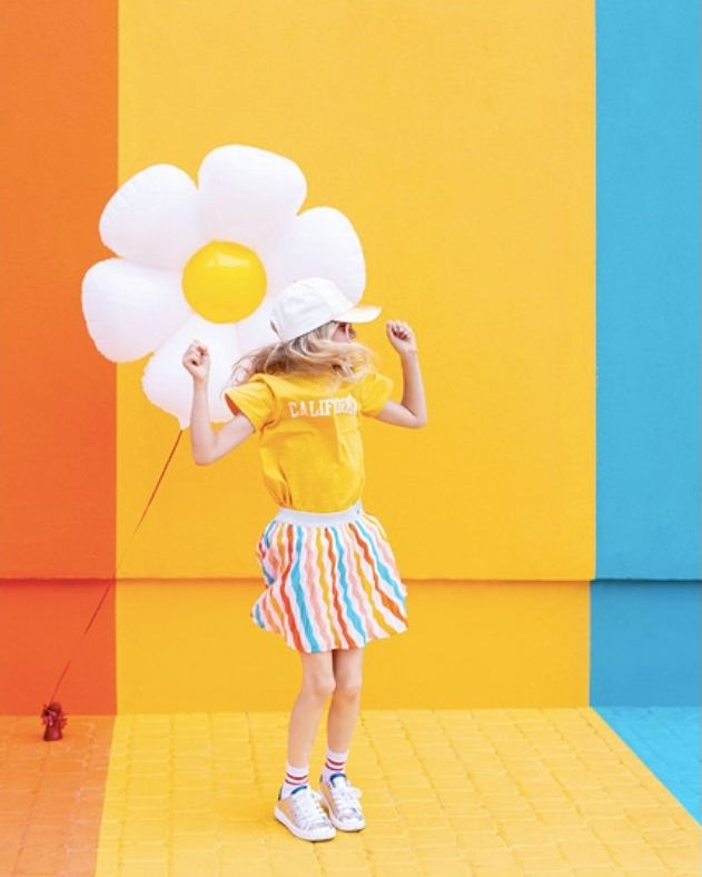 Person holding a large flower-shaped balloon against a colorful geometric background