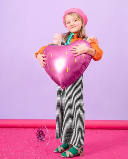 Child holding a strawberry-shaped balloon against a purple background